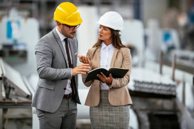 İşadamı ve iş kadını fabrikada iş konuşuyorlar.