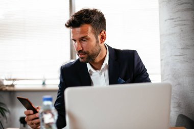 Genç iş adamı projeler üzerinde çalışıyor. Ofiste çalışan takım elbiseli yakışıklı bir iş adamı..