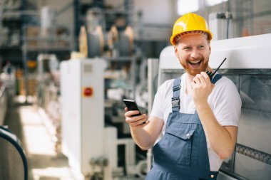 Sarı miğferli mutlu işçi fabrikada telefon kullanıyor. 