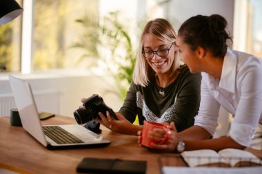 Ofiste iki kadın kameraya bakıyor ve köpekle oynuyor.