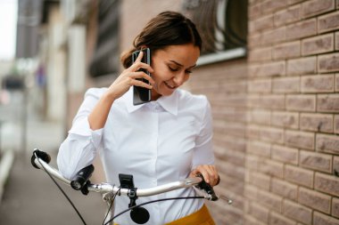Akıllı telefon kullanan bisikletli genç bir kadın.