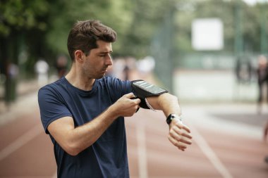 Genç adam antrenman sırasında kalp atışlarını kontrol ediyor. Genç adam atletizm pistinde egzersiz yapıyor..