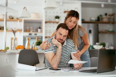 Yorgun çift mutfaktaki masada belgeleri inceliyor.