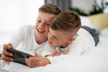 İki küçük kardeş telefonda oyun oynuyorlar. Güzel çocuklar evde eğleniyor..