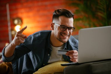 Genç adam oturma odasında online alışveriş için kredi kartı kullanıyor..