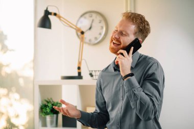 Ofiste akıllı telefon kullanan kızıl saçlı yakışıklı bir iş adamı.