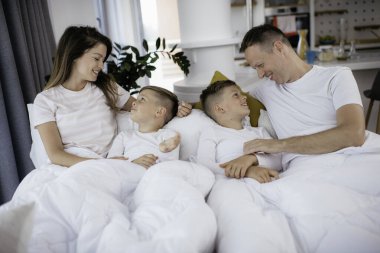 Genç bir aile yatakta eğleniyor. Oğulları yatakta dinlenen mutlu ebeveynler..