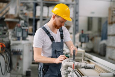 Üretim hattındaki fabrika işçisi. Fabrikada çalışan sarı kasklı adam..