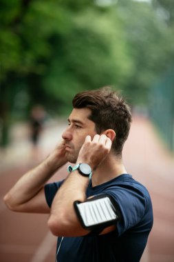 Genç adam antrenman sırasında kalp atışlarını kontrol ediyor. Genç adam atletizm pistinde egzersiz yapıyor..