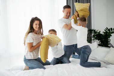 Oğulları yatakta yastıklarla savaşan genç ebeveynler. Mutlu anne ve baba ve oğlanlar evde eğleniyor..