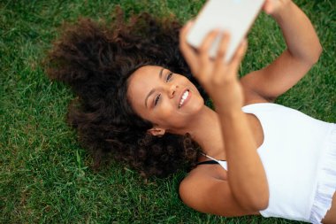 Güzel Afrikalı kız çimenlerde uzanıp selfie çekiyor.