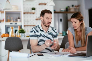Yorgun çift mutfaktaki masada belgeleri inceliyor.