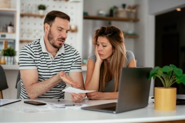 Yorgun çift mutfaktaki masada belgeleri inceliyor.