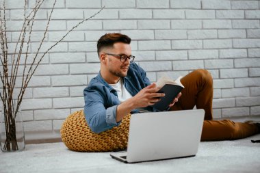 Genç yakışıklı adam yerde oturuyor ve kitabı okuyor..