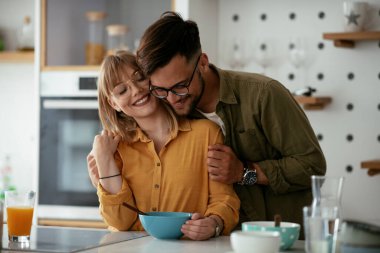 Genç çift evde kahvaltı hazırlıyor. Sevgi dolu çift mutfakta mısır gevreği yiyor..