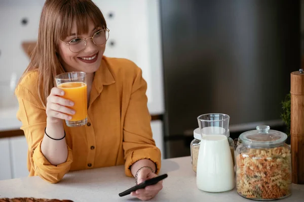 Wanita Cantik Minum Jus Jeruk Dapur Dan Menggunakan Smartphone — Stok Foto