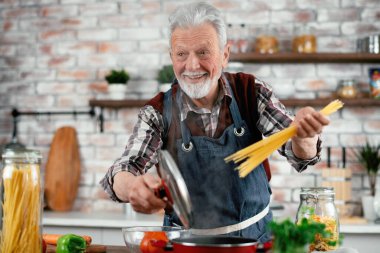 Yaşlı adam yemek yapıyor. Mutfakta kıdemli adam var..