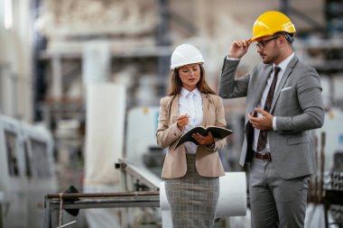 İşadamı ve iş kadını fabrikada iş konuşuyorlar.