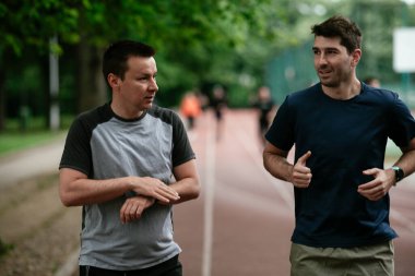 Gençler yarış pistinde antrenman yapıyor. İki genç arkadaş atletizm pistinde koşuyor.