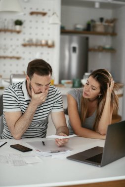 Yorgun çift mutfaktaki masada belgeleri inceliyor.