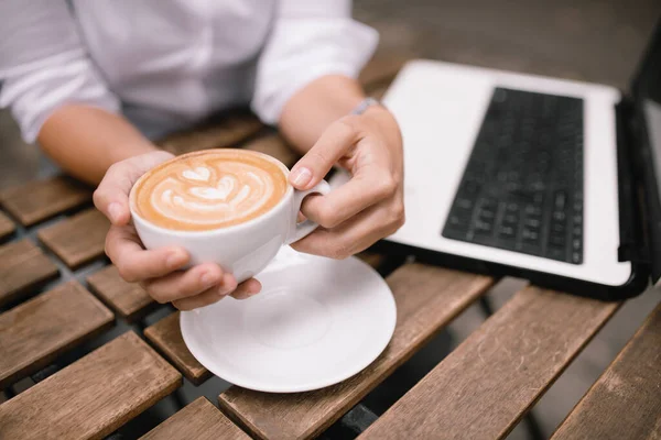 Woman sitting at cafe with laptop. Female hand on laptop and cup of coffee.