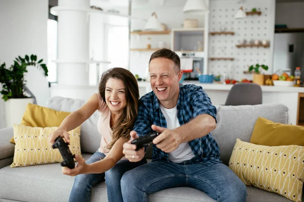 Boyfriend and girlfriend playing video game with joysticks in living room. Loving couple are playing video games at home.