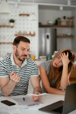 Yorgun çift mutfaktaki masada belgeleri inceliyor.