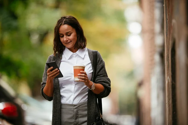 Young woman walking with phone and coffee on the street