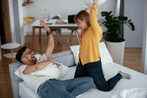 Erkek arkadaş ve kız arkadaş yatakta yastık kavgası yapıyor. Mutlu çift evde eğleniyor.