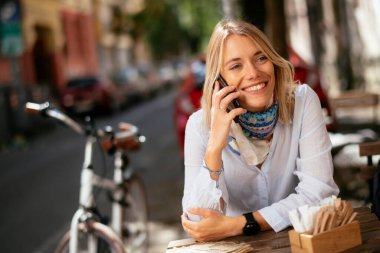 Kafede telefonla konuşan ve bilgisayarla çalışan genç ve güzel bir kadın..
