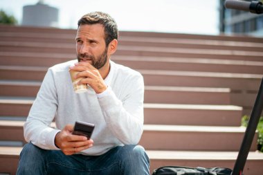 Yakışıklı genç işadamı telefon kullanıyor ve sokakta kahve içiyor.