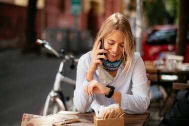 Kafede telefonla konuşan ve bilgisayarla çalışan genç ve güzel bir kadın..