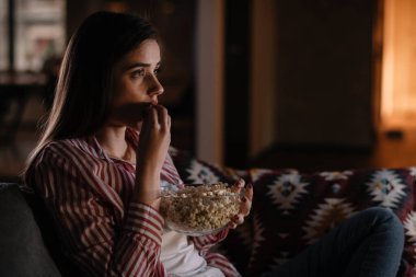 Gece film izleyen güzel bir kadın evdeki oturma odasında bir kanepede oturuyor.