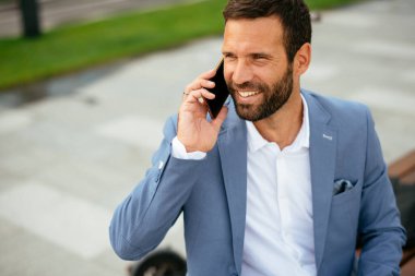 Genç işadamı sokakta çalışırken telefonla konuşuyor.