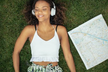 Genç Afrikalı kız çimlere uzanıp müzik dinliyor.