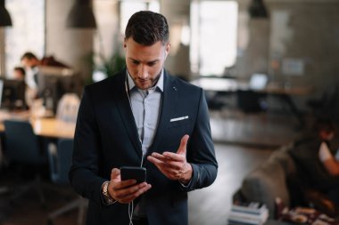 Takım elbiseli yakışıklı iş adamının portresi. Ofiste telefonla müzik dinlemek.