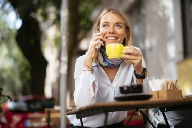 Kafede telefonla konuşan ve bilgisayarla çalışan genç ve güzel bir kadın..