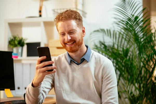 Joven Jengibre Hombre Negocios Riendo Oficina Mientras Utiliza Teléfono Imagen de archivo