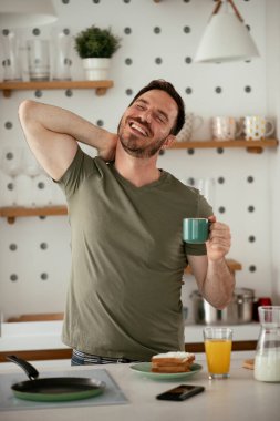 Yakışıklı adam mutfakta kahve içiyor ve esniyor. Genç adam sabah eğleniyor..
