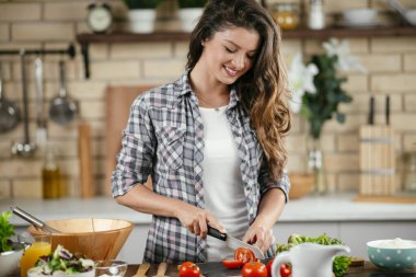 Gülümseyen kadın mutfakta yemek yapıyor.