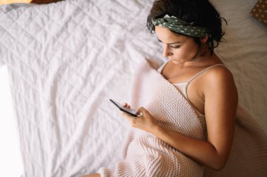 Yatakta telefon kullanan genç ve güzel bir kadın. Yatakta yatan kız..