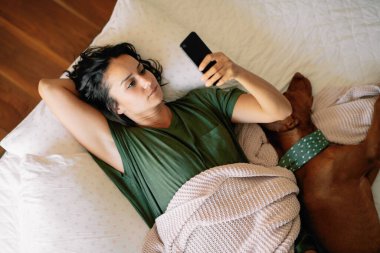 Yatakta telefon kullanan genç ve güzel bir kadın. Yatakta yatan kız..