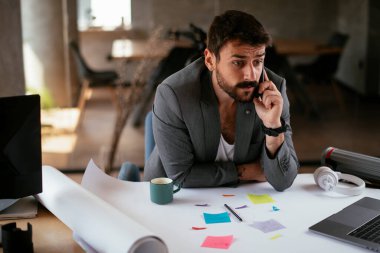 İş adamı proje üzerinde çalışıyor. Genç işadamı ofiste akıllı telefondan konuşuyor..