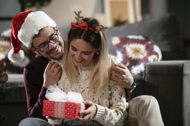Genç adam ve kız arkadaşı Noel süslemeli oturma odasında hediye kutusuyla