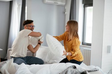 Erkek arkadaş ve kız arkadaş yatakta yastık kavgası yapıyor. Mutlu çift evde eğleniyor.