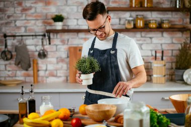 Mutfakta önlük giyen genç adam yemek pişiriyor.