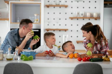 Anne ve baba oğullarla kahvaltı hazırlıyorlar. Genç bir aile mutfakta lezzetli yemekler hazırlıyor ve eğleniyor.