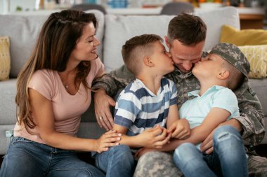 Mutlu asker ailesiyle birlikte yerde oturuyor. Asker ve karısı evde çocuklarla eğleniyor.