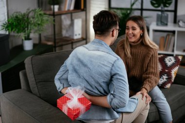 Genç adam ve kız arkadaşı oturma odasında hediye kutusuyla