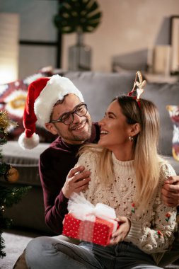 Genç adam ve kız arkadaşı Noel süslemeli oturma odasında hediye kutusuyla